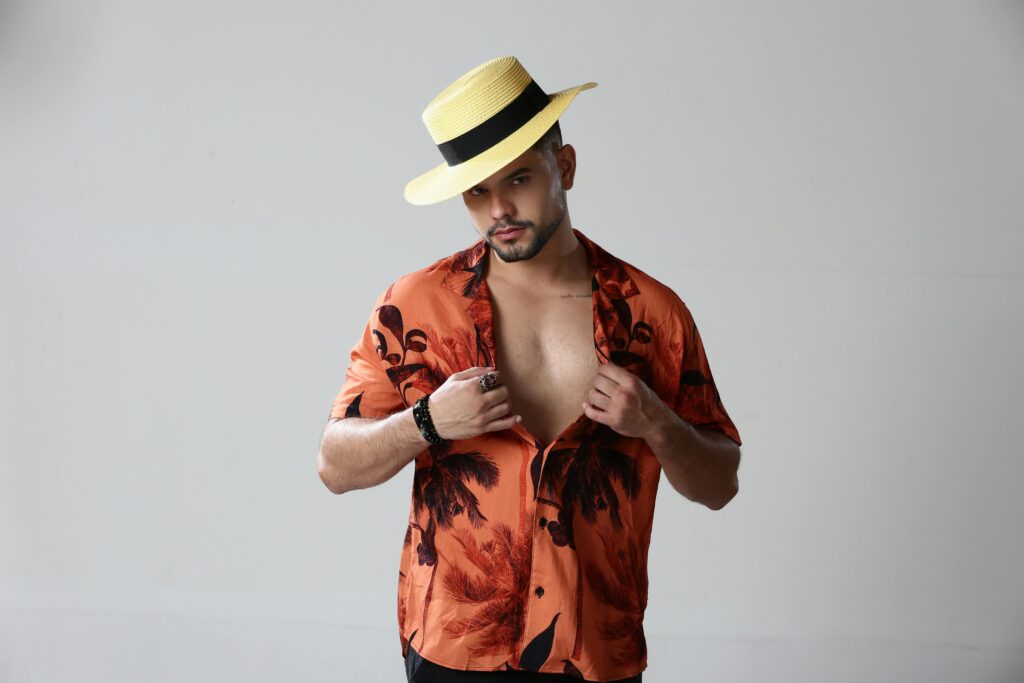 Confident man posing in a Hawaiian shirt and straw hat against a white background.