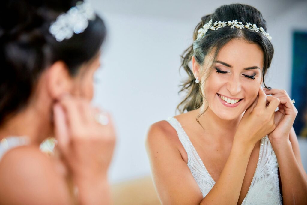 A smiling bride adjusts her earrings in an elegant pose, radiating happiness and beauty.