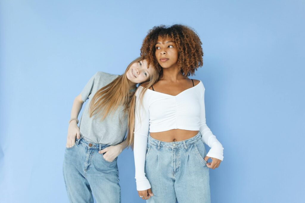 Two stylish women posing together against a blue backdrop, embracing friendship and fashion.